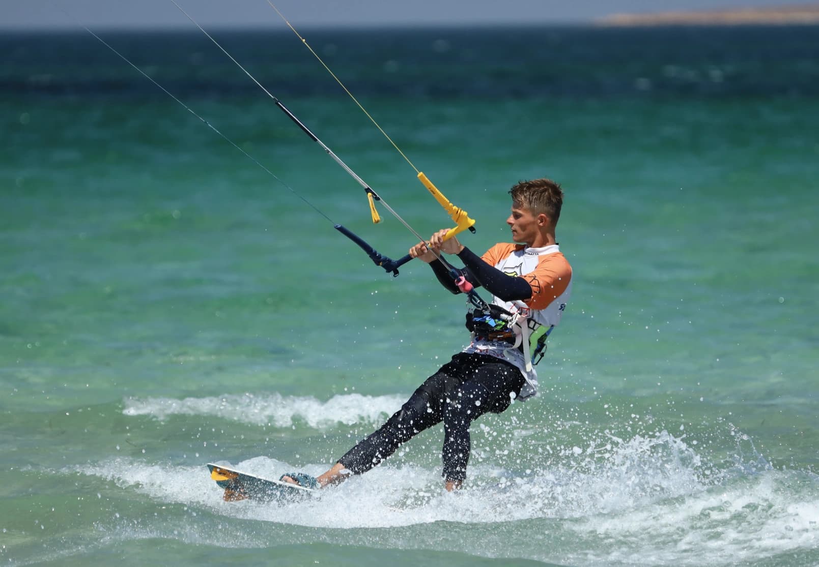 Un kitesurfeur navigue au-dessus de l’eau turquoise.