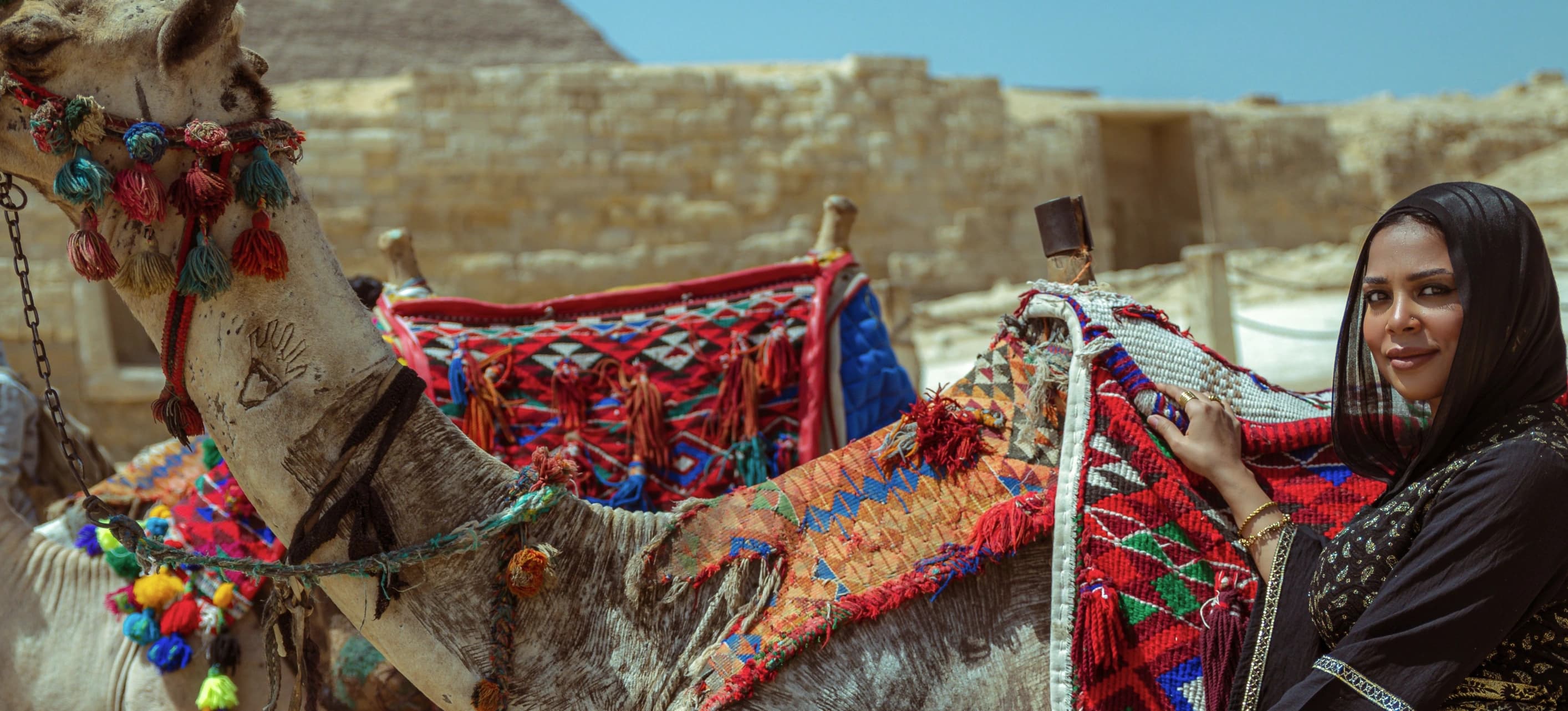 Une voyageuse près d’un dromadaire aux étoffes colorées, en Égypte